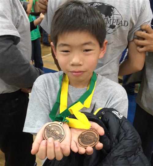 A child is holding his two Science Olympiad Medals 